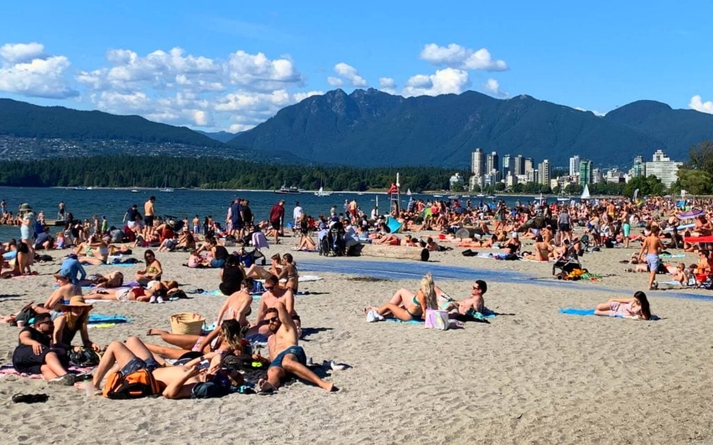 people suntanning at kits beach in vancouver with downtown and mountains