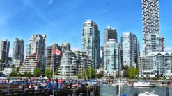 busy outdoor plaza in front of granville island with vancouver skyline in background