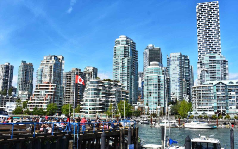 busy outdoor plaza in front of granville island with vancouver skyline in background