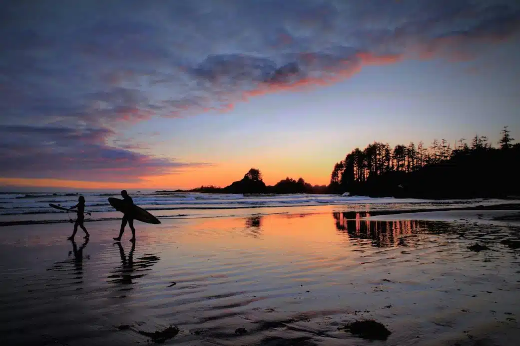 A couple surf at Chesterman Beach in Tofino, BC.