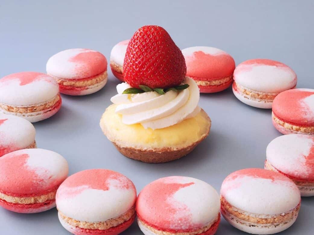 custard cake with whipped cream topped with strawberry fruit surrounded by pink and white macarons at bon macaron