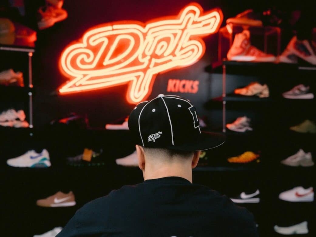showing a man's back wearing a black tshirt and black cap showcasing the dipt signage in neon red and sneakers displayed on racks for shopping granville street