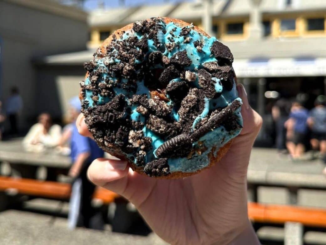 a hand holding a blue donut with crushed oreos on top at granville island