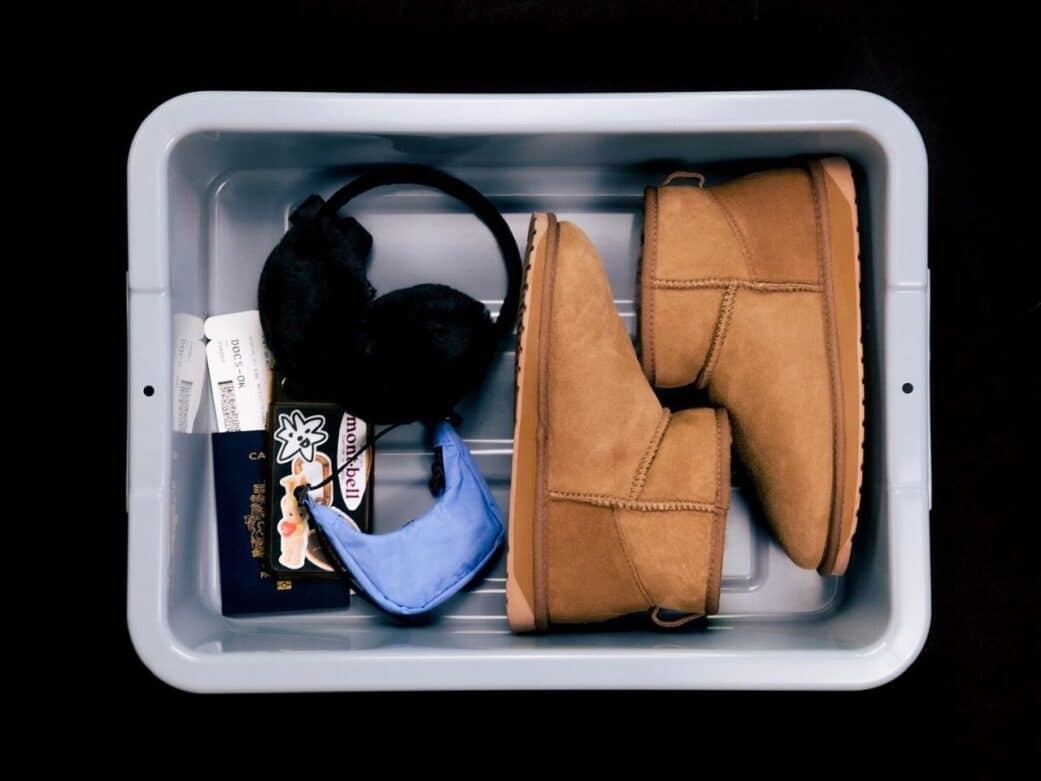 a gray bin containing brown boots, black earmuffs, a lavender bag and passport